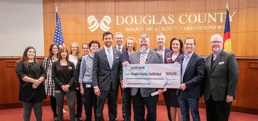 U.S. Rep. Jason Crow, second from right, stands with Douglas County Commissioners Lora Thomas (left of Crow), George Teal (left of Thomas) and Abe Laydon (left of Teal) in the foreground of the photo next to a ceremonial check for funding for mental health services in Douglas County at a March 20 news conference. Standing with them are leaders in providing mental health services in the county.