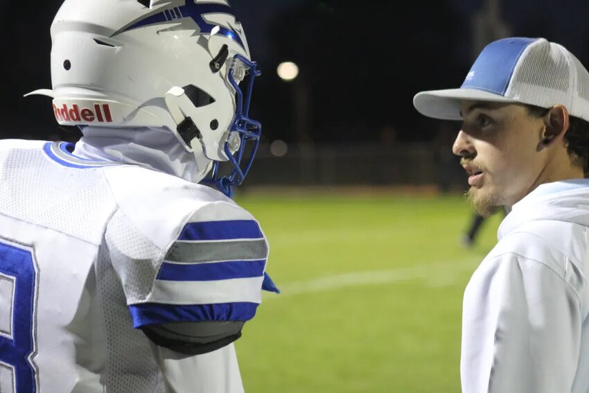 Fort Lupton assistant coach RJ Ramirez chats with player Frankie Flores during the Bluedevils’ homecoming win against Valley High School on Sept. 15 / Steve Smith
