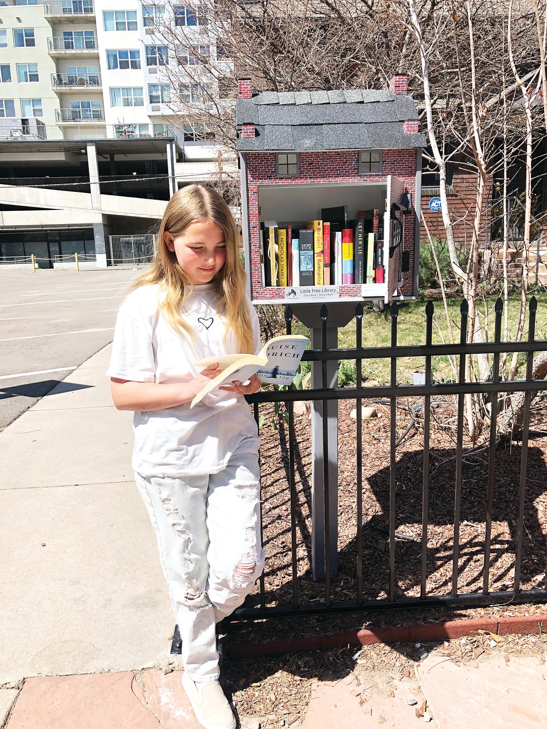 Maggie Carabello, 11, reads a book she found inside the new Little Free Library outside of the Denver Woman&rsquo;s Press Club at 1325 Logan St. in Denver&rsquo;s Capitol Hill neighborhood. Carabello and her grandfather were on their commute home to Virginia Village from the Denver Center of Performing Arts when Carabello saw the Little Free Library and asked her grandfather to stop so she could get a book for herself.