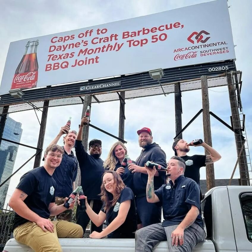 The Dayne's crew celebrates in front of a congratulatory billboard.