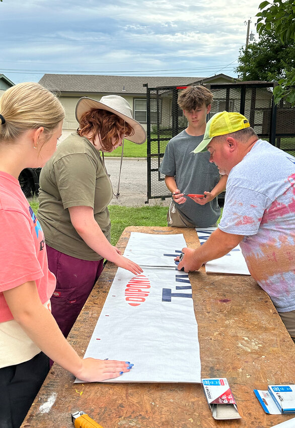 L-R Sydney Byrd, Claire O’Donald, Luke Brown assist and learn as Joel Robbins measures and cuts material.