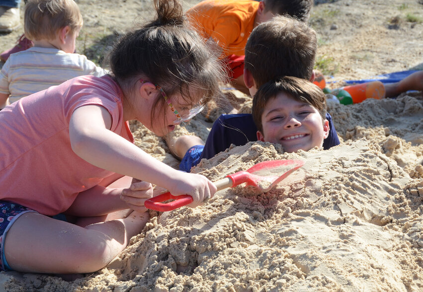 Ellie Caron buries a giggling Brady Broussard in the sand box.