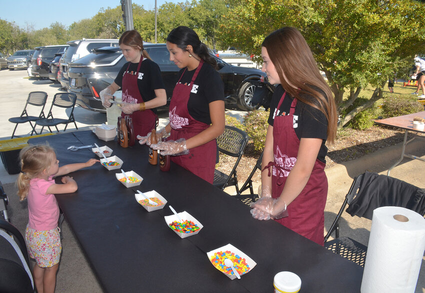 Volunteers Alanna Rogers, Mackenzie Griffith and Adeline Gustavson help 3-year-old Emma Sides decorate apple slices with candy sprinkles.