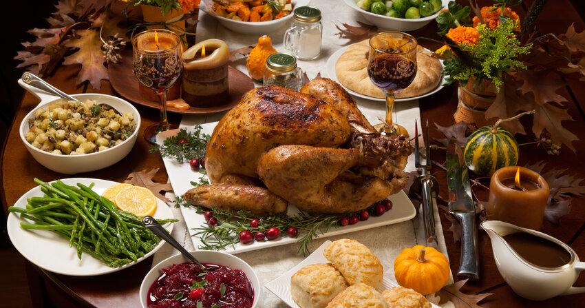 Roasted turkey garnished with cranberries on a rustic style table decoraded with pumpkins, gourds, asparagus, brussel sprouts, baked vegetables, pie, flowers, and candles.
