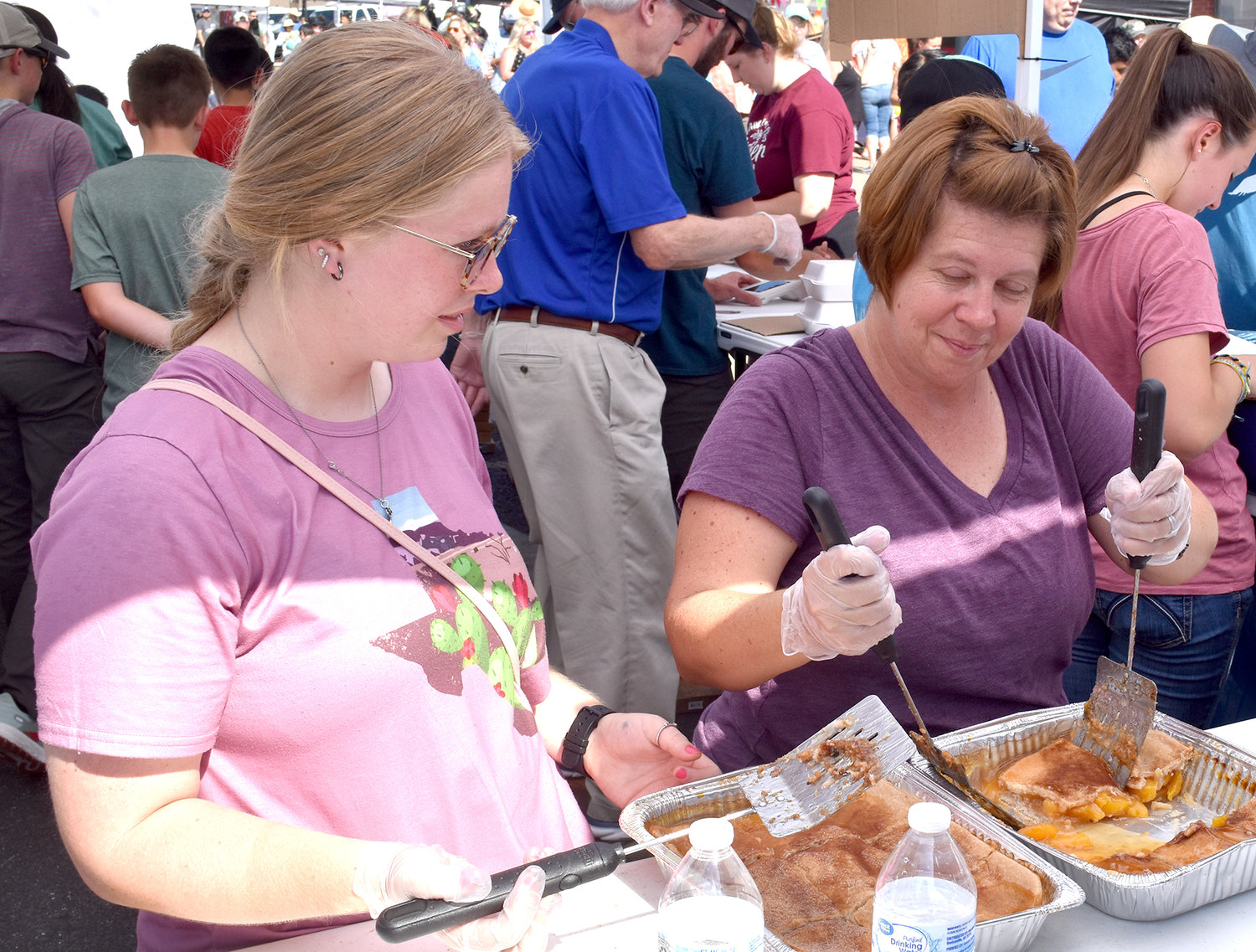 Rylin Ray (left) and Mendy Holaway dished out servings of peach cobbler at the Weatherford Optimist Club booth. About 2,700 servings were sold before the day was complete.