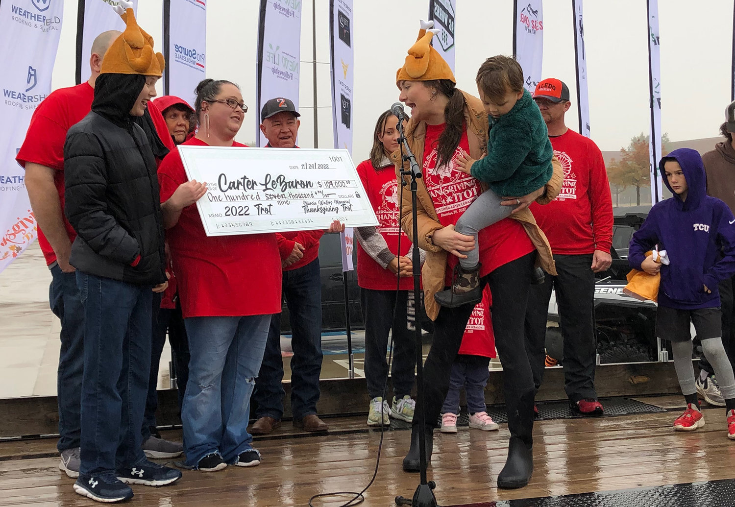 Carter LeBaron and his family react when presented with a check for $109,000, the proceeds from this year's Marcia Walters Memorial Thanksgiving Trot. Shown also are event co-chair and emcee Nikki Thompson and son, Tagg.