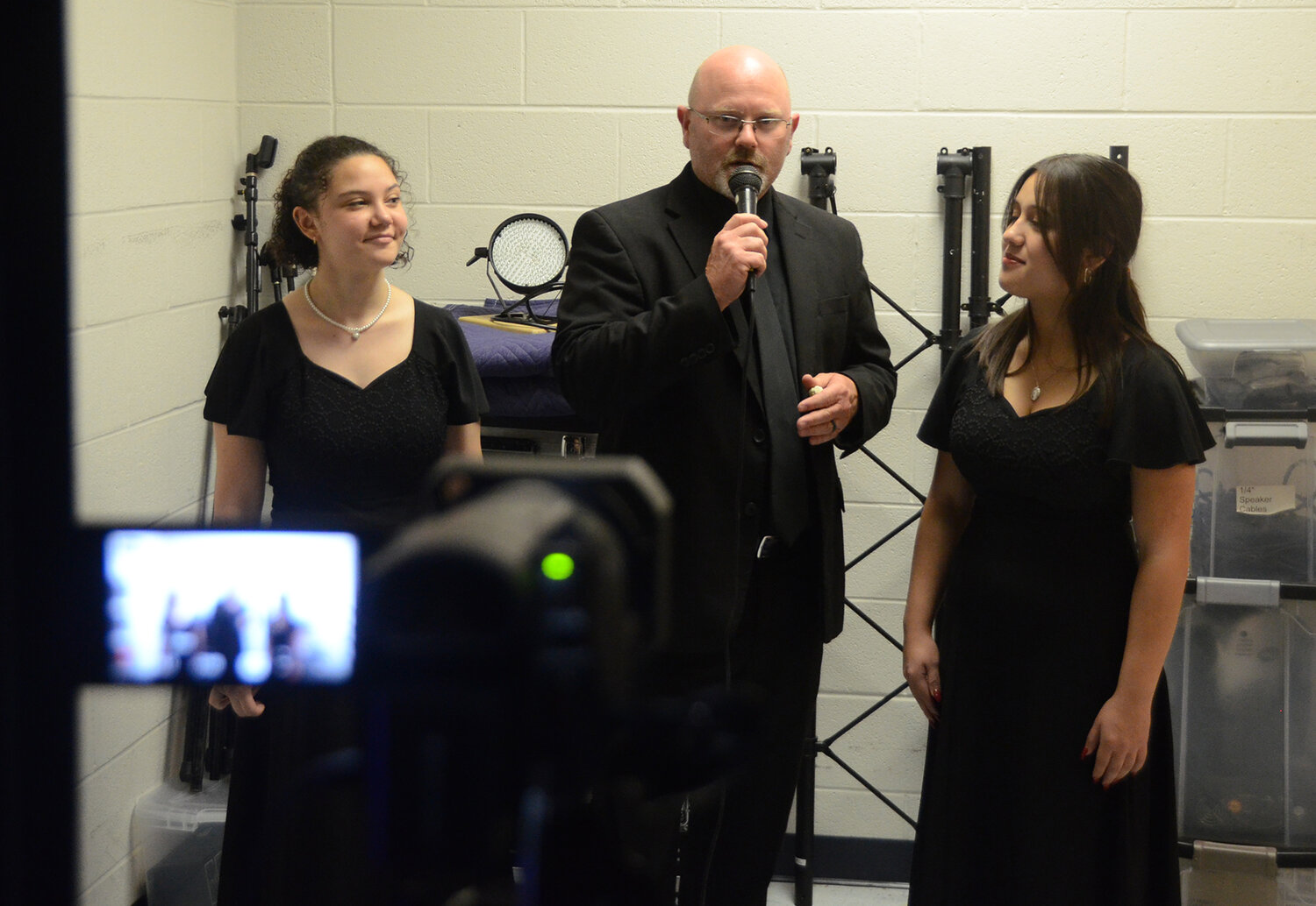 Aledo Band Director Jacob Albin speaks with choir members Victoria Duffey and Katie Curran backstage as the interview appears on stage for the pre-event audience to enjoy.