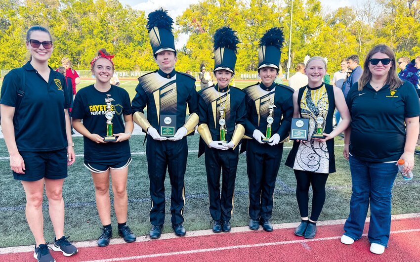 Director Lisa Dobbs, percussionist Kate Hutchinson, drum majors Thomas Elliott, Hayden Sage, and Amaya Burchett, color guard captain Kayleigh Friebe, and director Elizabeth Betts pose with the Fayette band’s multiple trophies following the award ceremony on Saturday afternoon.