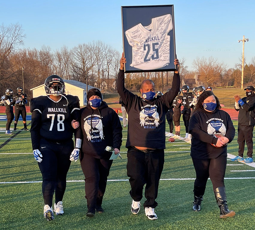 Otto Smith, the father of Wallkill football player Miguel Lugo, who died after practice on March 1, holds up Lugo&rsquo;s jersey signed by the team. He is flanked by Lugo&rsquo;s brother, A&rsquo;Kell Smith, his mother, Mallisa Smith and sister Nataleigh Williams before the Panthers&rsquo; game against Minisink Valley on Friday night.