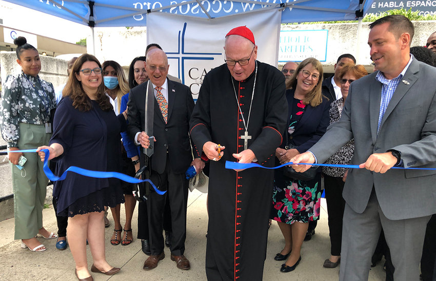 Shannon Kelly, CEO of Catholic Charities of Orange, Sullivan, and Ulster Counties holds the ribbon as Timothy Cardinal Dolan cuts the ribbon for the new office space with the help of Orange County Executive Steve Neuhaus holding the other side of the ribbon.
