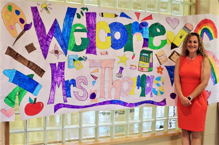 Jenna Thomas stands beside a colorful welcome sign, indicating her appointment as the new Principal of the Marlboro Elementary School.