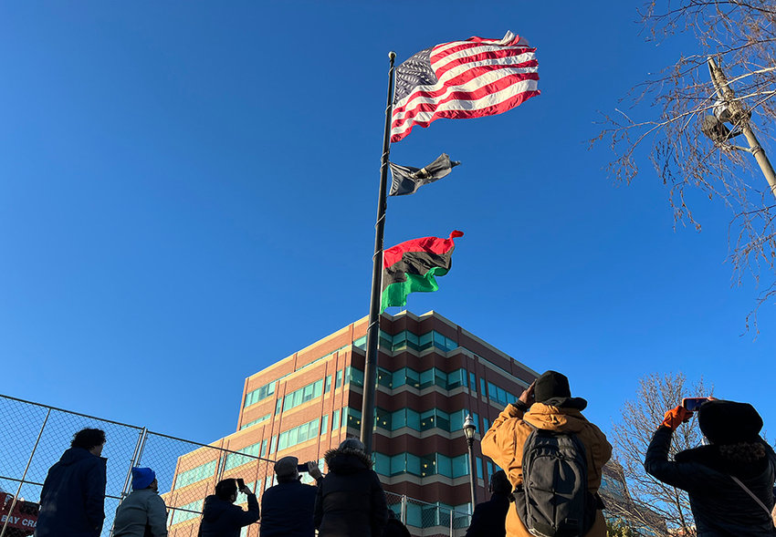 Community members take videos and photos as the Pan-African flag is raised in the city.