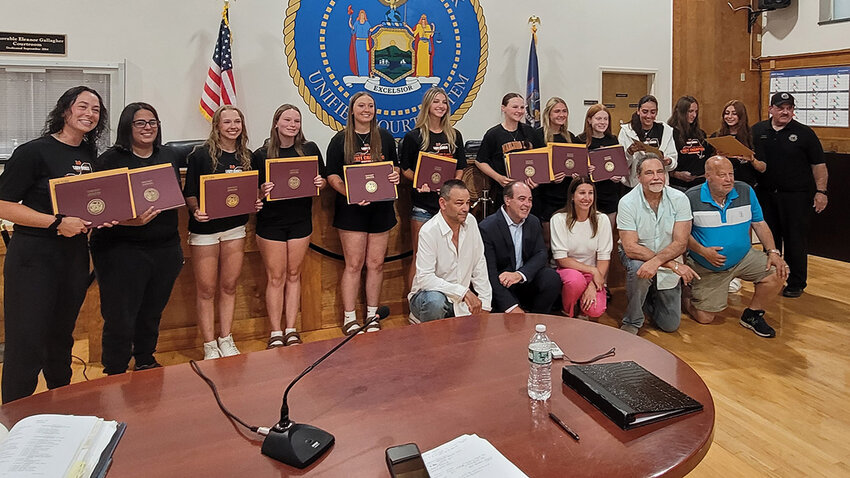Members of the Lady Dukes and their coaches are all smiles after they received several awards at the June 24 Town Board meeting. Shown (L-R) are Coach Andrea Schoonmaker, Assistant Coach Christina DeNatale, Kalista Birkenstock, Madison Gibney, Leah Gunsett, Katelyn Gordon, Emily Hite, Emma Jackson, Lily Sullivan, Mia Verdi, Taylor Castellani and Sam Maleck, along with County Legislator Tom Corcoran. Kneeling are: Board member Dave Zambito, Town Supervisor Scott Corcoran, and board members Sherida Sessa, Manny Cauchi and Ed Molinelli. Not in photo were Jaylene Valentine, Katie Mole, and Kiera Del Salto.