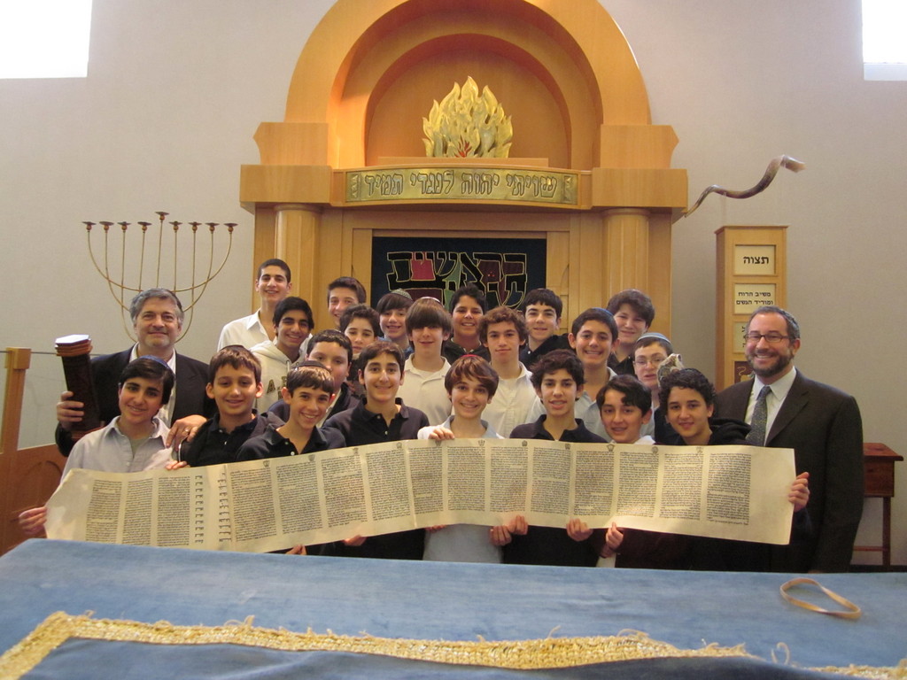 Dr. Paul Brody (2nd row, left) with his North Shore Hebrew Academy Middle School students and principal, Rabbi Jeffrey Kobrin. (The Megillah shown was presented to Dr. Brody by Rabbi Yitzchak Dovid Grossman, known as the &ldquo;Disco Rabbi,&rdquo; in appreciation of Dr. Brody&rsquo;s dedication to the Migdal Ohr Institutions in the Galil.)