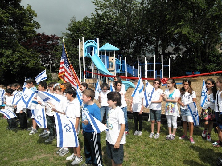 Photo by Sergey Kadinsky  Students of the Bradeis School gather in Lawrence in a patriotic display at the ribbon cutting of their new playground. The event remembered the Fogel family of Itamar and two longtime supporters of the school.