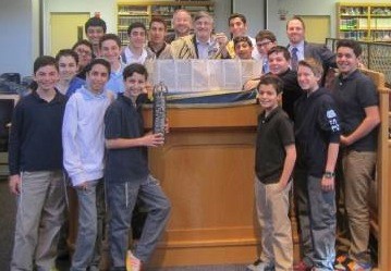 North Shore Hebrew Academy Middle School will reach a mile-stone when 16 Ashkenazic and Sephardic students read Megillat Esther for their schoolmates and faculty on Purim day, Sunday, March 16. Dr. Paul Brody of Great Neck (wearing tallit) has instructed close to 200 students over the past 13 years at NSHA, enabling them to read the Megillah at synagogues, hospitals, nursing homes and private homes for those unable to attend synagogues for the megillah reading. NSHA