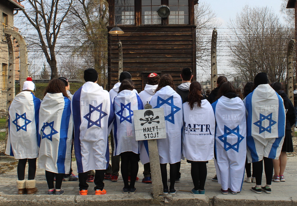Students wrapped in Israeli flags at a concentration camp fence during HAFTR HS trip.