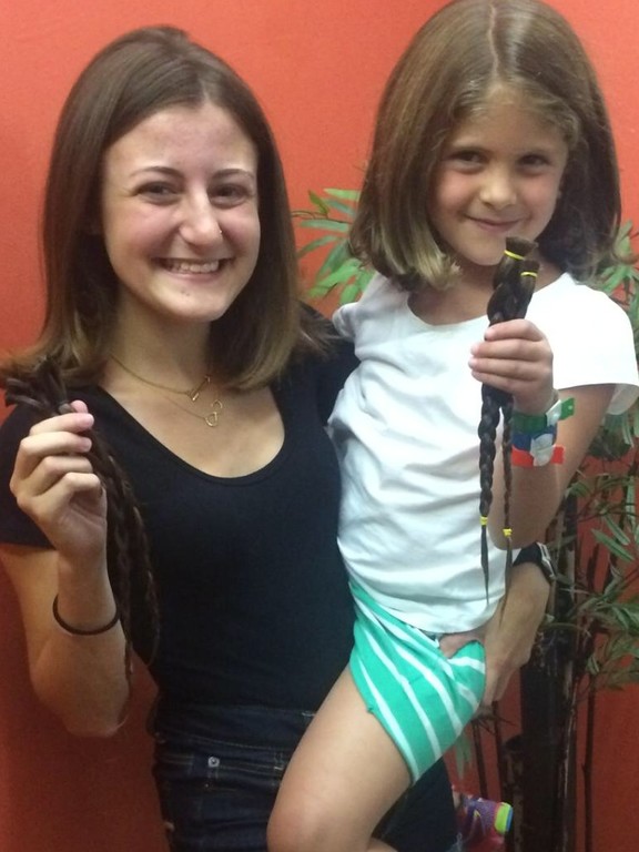 Rachel Schreiber, left, and cousin Kayla Hercman hold their freshly shorn braids to be donated to Zichron Menachem in Israel. The hair donations will be made into wigs for children who have lost their hair to cancer.