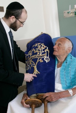 Rabbi Rachmiel Rothberger hands the 1880 torah scroll to Arthur Fisher, a patient at Calvary Hospital