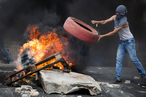 Palestinian rioter throws a tire into a fire, blocking a road during clashes with Israeli police in eastern Jerusalem on Oct. 7.