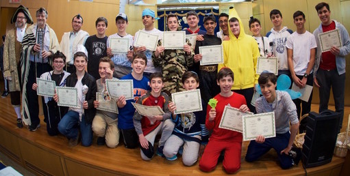 North Shore Hebrew Academy Head of School Rabbi Jeffrey Kobrin (top left); Dr. Paul Brody of Great Neck (holding megillah container), and NSHA Middle School Principal Rabbi Adam Acobas. Student Danny Kroll (front row, third from left) &ldquo;hangs&rdquo; a composite of modern day Hamans. Each year, Brody trains the students to read the Megillah Esther.