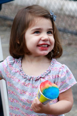 Two-year old Abigail Lazarus delights in her rainbow snowcone at Sunday&rsquo;s Kulanu Fair at Andrew J. Parise Park in Cedarhurst.