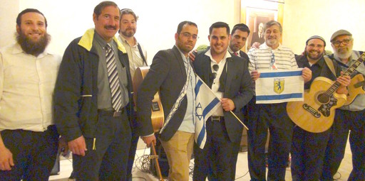 Pictured in the Saffra Synagogue (from left): organizer Dr. Joe Frager, chairman (second from left), chairman Dr. Paul Brody (holding flag of Yerushalayim), singing star Tal Vaknin (with Israeli flag) who coordinated with Israeli pianist Shlomi Aharoni (behind him), and Mati Shriki (holding guitar near left), guitarist &ldquo;Mr. Shabbos&rdquo; Josh Alpert (second from right) and his band White Shabbos, consisting of drummer Pesach Alpert (far left), bassist Mordechai Harrison (back row) and Noam Segal (far right) on mandolin. Avi Kilimnick (not shown), a rising singing star from Rochester, provided the high notes.