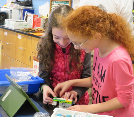 Two HANC students are learning to build a robot with Legos that has a sensor attached to it.