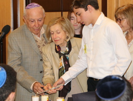 Manhattan Day School eighth grader Levi Langer accompanies survivors Garay and Lucy Lipiner in lighting candles in memory of their families who were murdered at the hands of the Nazis.
