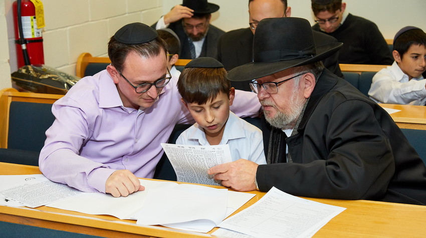 Meir Katz, a fifth grader at Yeshiva of South Shore, is accompanied by his father and grandfather at a multi-generational celebration of his class&rsquo; Haschalas Gemarah.