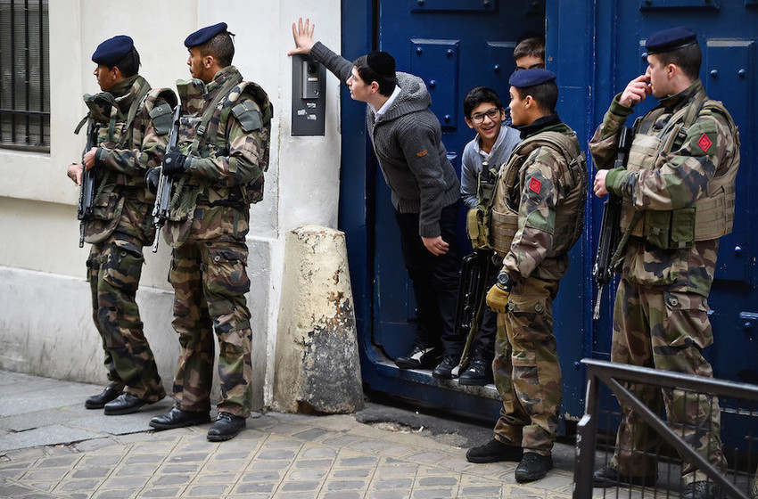 Children look out from a doorway as armed soldiers patrol outside a School in the Jewish quarter of the Marais district of Paris on Jan. 13, 2015.