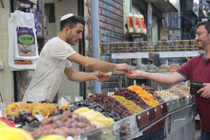 A dried fruit and nut seller gives change to a customer in Jerusalem&rsquo;s Mahane Yehuda market.