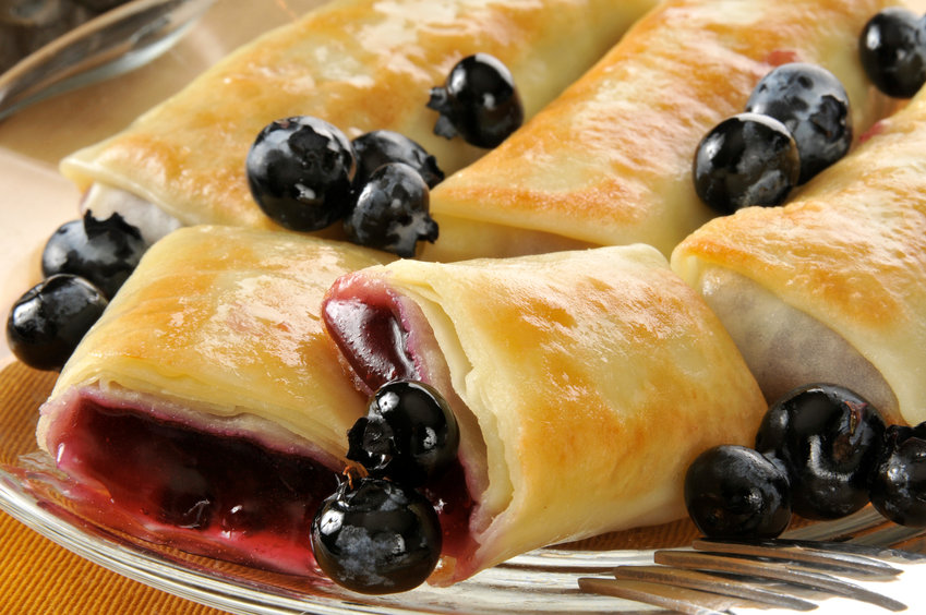 Closeup of golden blueberry blintzes or crepes with fresh berries.