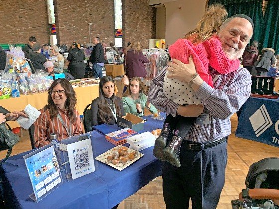 Cahal Executive Director Shimmie Ehrenreich embraces a granddaughter while event organizer Rina Hirsh looks on at Sunday's Cahal Chanukah Boutique at HANC ECC in West Hempstead.