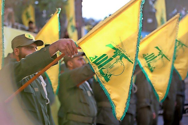 Flags of Hezbollah fly during a funeral salute.