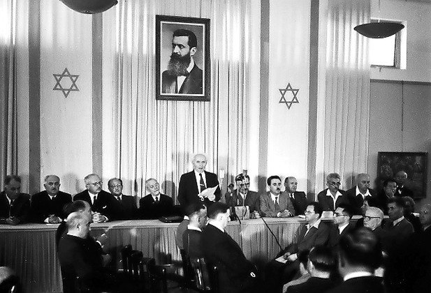 Israeli first prime minister David Ben-Gurion declares independence beneath a portrait of Theodor Herzl, founder of modern Zionism.
