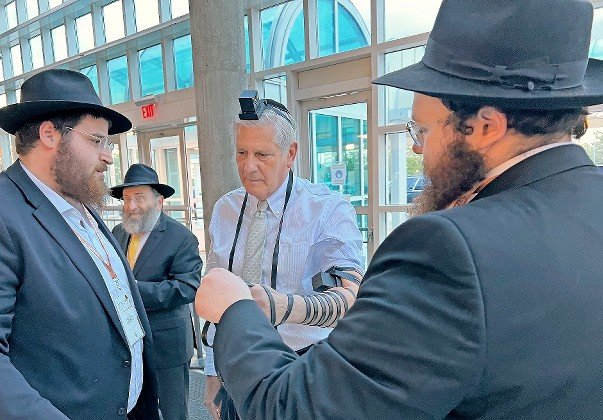 Nassau County Executive Bruce Blakeman wraps tefillin with Rabbis Mendel Wolowik and Mendel Gordon, as Rabbi Anchelle Perl looks on.