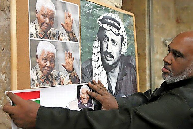 A Palestinian man hangs a picture of Nelson Mandela next to a poster of Yasser Arafat, in Jerusalem&rsquo;s Old City on Dec. 8.