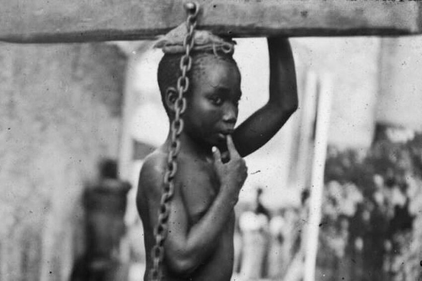 A photograph of an enslaved boy in Zanzibar, circa 1890. The original image states: &quot;An Arab master's punishment for a slight offense.&quot;