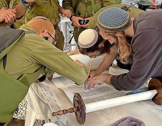 IDF soldiers add their letters to the Torah scroll at a base on the Gaza border.