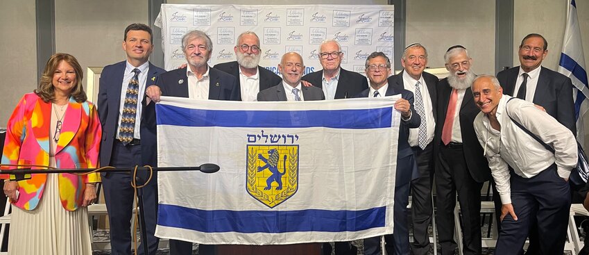 Officers and executives of the organization are pictured behind a Jerusalem flag, from left: Shoshana Hikind, Dr. Gene Berkovich, Dr. Paul Brody, Mati Dan HaCohen, Chaim Leibtag, Rubin Margules, Robert Koppel, Dr. Jonathan Halpert, Dr. Steven Rubel, Daniel Luria, and Dr. Joseph Frager.