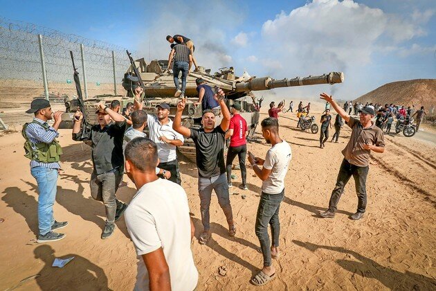 Palestinians take control of an IDF tank after breaching the Israeli border fence from Khan Yunis in the southern Gaza Strip, Oct. 7, 2023.