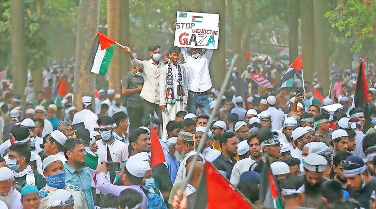Young men stand above the crowd holding a Palestinian flag and a &ldquo;Stop Genocide in Gaza&rdquo; sign during a rally in Dhaka, Bangladesh on April 12.