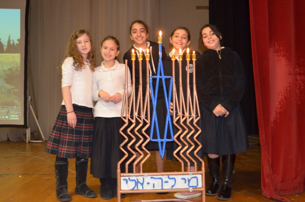 Five Shulamith students bask in the glow of the Chanukah lights at a school assembly.