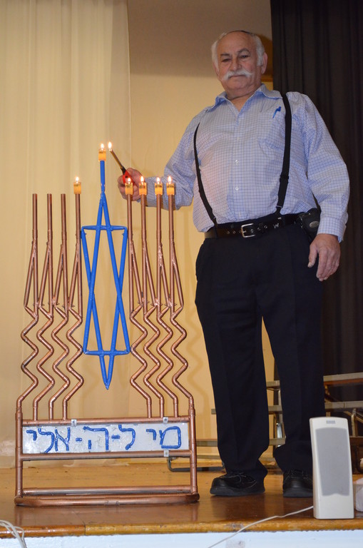 Gideon Gur Aryeh lights the   copper pipe menorah he created, on the stage at Shulamith School for Girls in Flatbush.