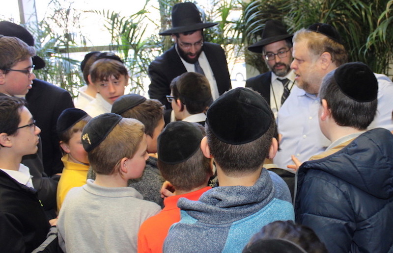 Yanky Brach is greeted by students after the surprise presentation at Yeshiva Darchei Torah. From right: Brach; Rabbi Dovid Frischman, menahel of YDT’s middle school; and Rabbi Avrohom Bender, a rebbi and menahel at YDT.