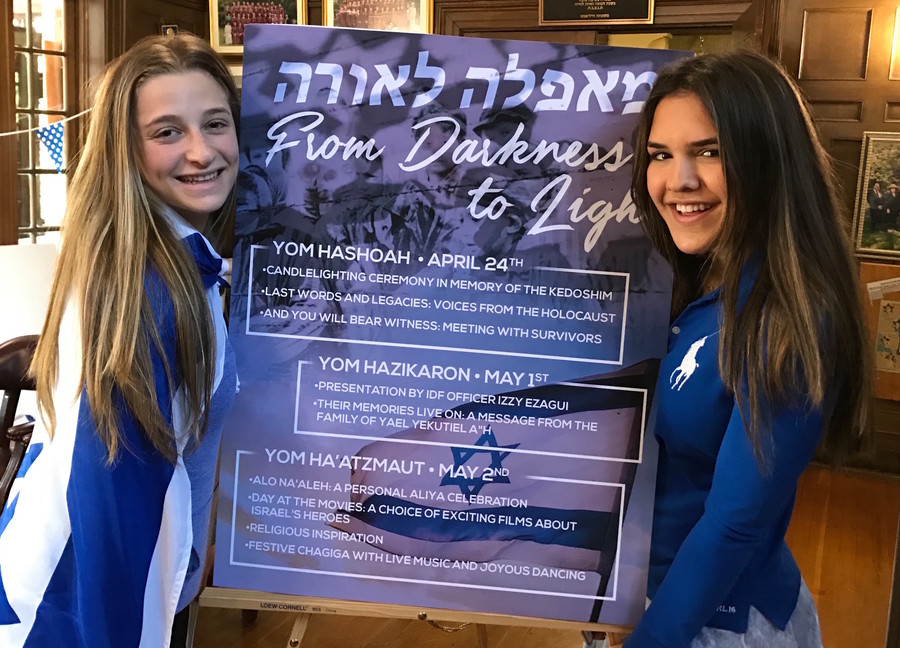 SKA girls flank a poster that explains the 3 days: Yom HaShoah, Yom Hazikaron, and Yom HaAtzmaut.