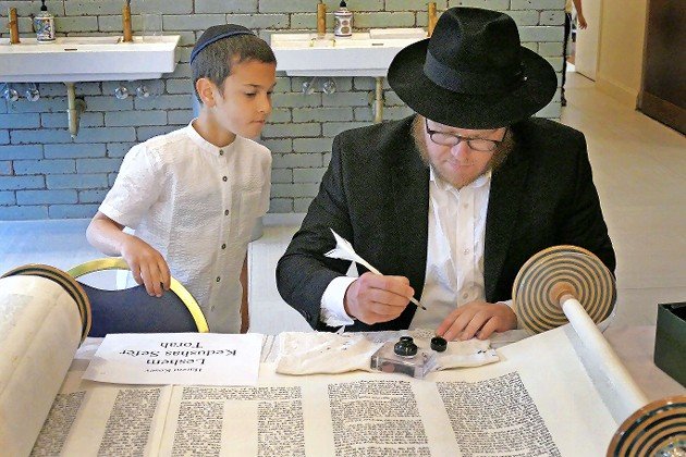 Moshe Goodman watches as finishing touches are applied to the Torah by Rabbi Chilik Weinfeld.