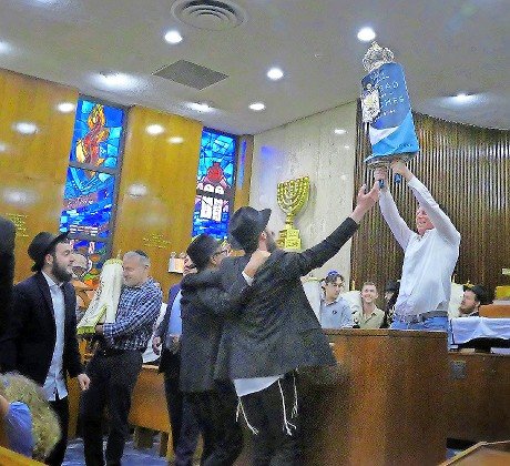 In the santuary, Philip Osrove lifts the Torah high into the air.