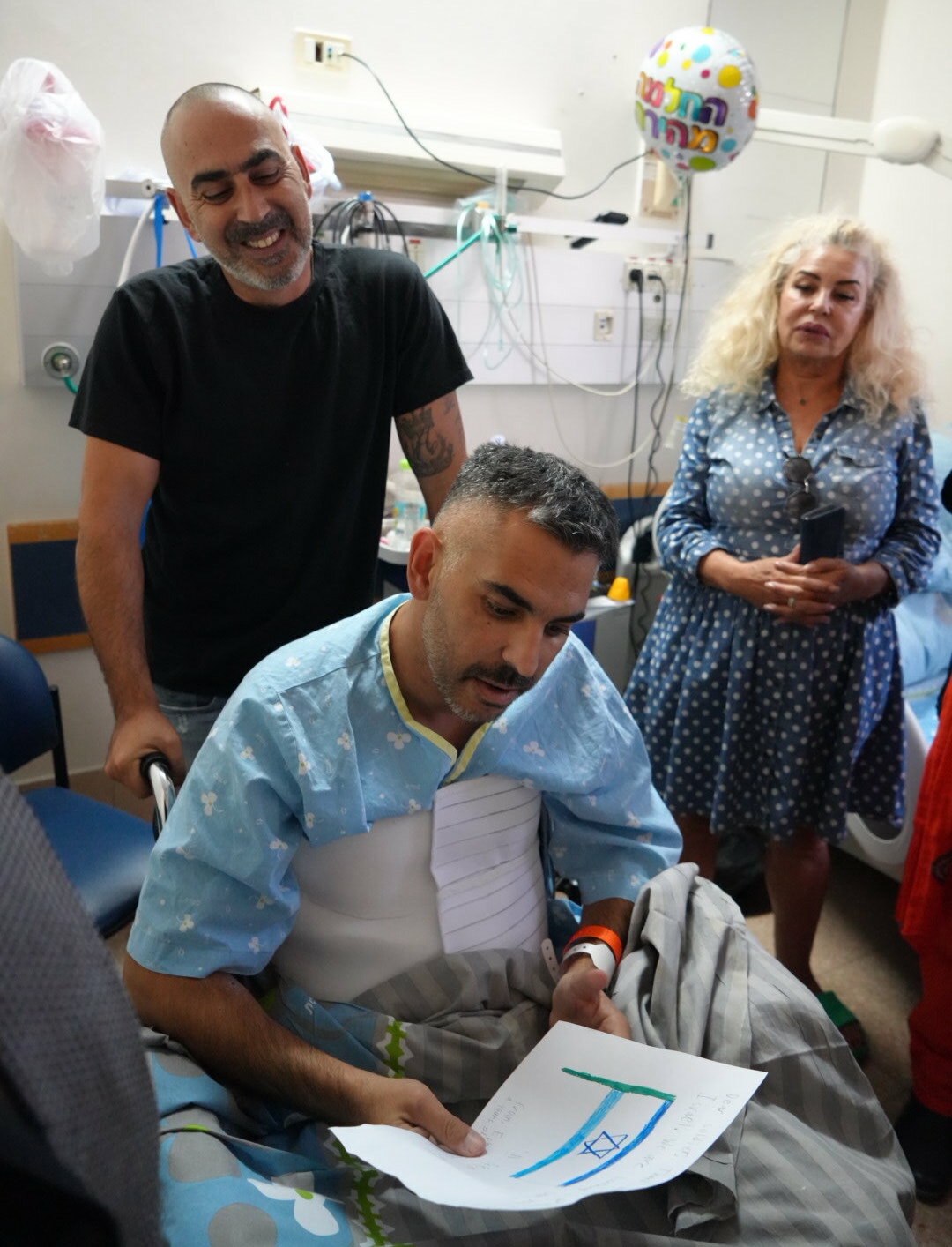 An IDF soldier wounded in battle recovering in Soroka hospital reads cards from American community members together with his family.